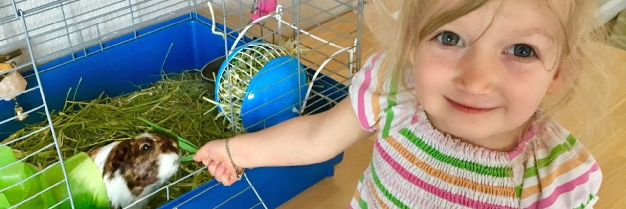 How Our Pet Helped Our Preschooler Understand Her Food Allergies A little blonde girl is looking at the camera while she feeds her small guinea pig.