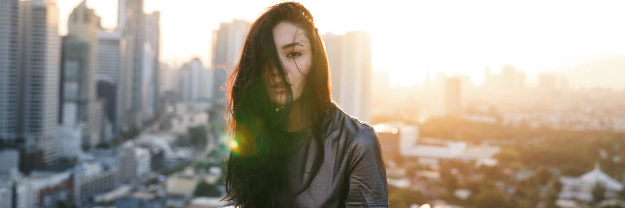 My Schizoaffective Disorder Diagnosis Does Not Define Me woman with brown hair over half her face looking into camera with NYC behind her