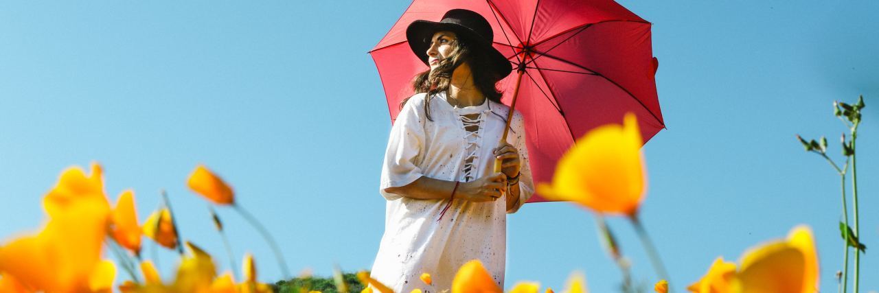 Finding Good Things in My Life With Bipolar Disorder photo of blonde woman in white dress standing in field of yellow flowers, holding a red umbrella under blue skies