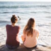 Two young women sit looking out over the ocean