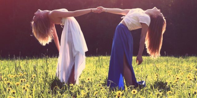 What to Know About Finding Trust Again After Toxic Relationships photo of two women in meadow holding each other's hands, facing each other and leaning back away from each other