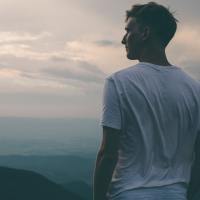 man in a white t shirt standing looking out into the sky and mountains