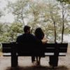 couple sitting on a bench outside in a park, arms around each other