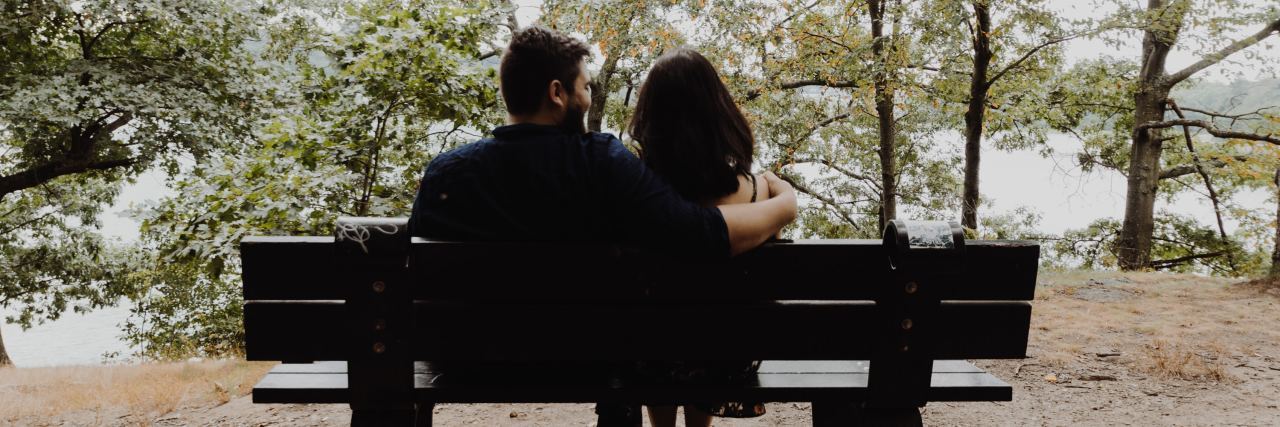 couple sitting on a bench outside in a park, arms around each other