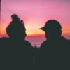 photo of couple side by side and silhouetted by vibrant sunset