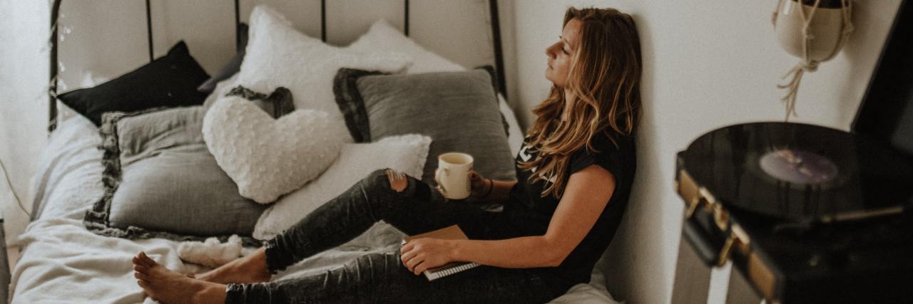 The Struggle of Living With Depression and Anxiety in College young woman sitting on bed with her back against the wall holding a cup of coffee
