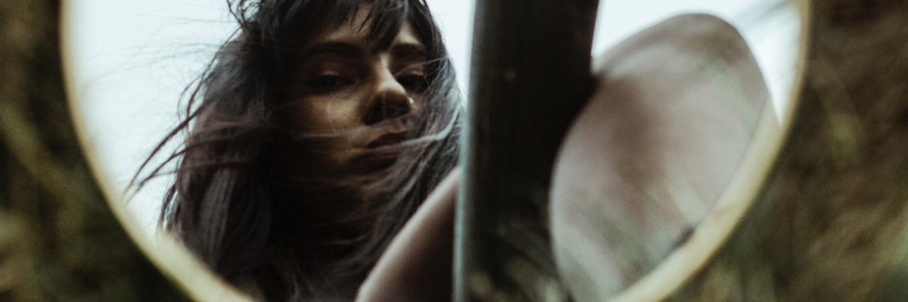 Eating Disorder Recovery Means Discovering My Identity photo of young woman looking at her reflection in circular mirror on grass