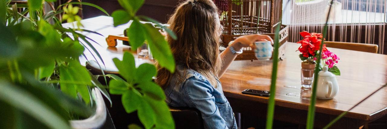 Why Detoxing Won't Work and Is Dangerous for Eating Disorders photo of woman sitting in cafe with green plants in foreground, drinking tea