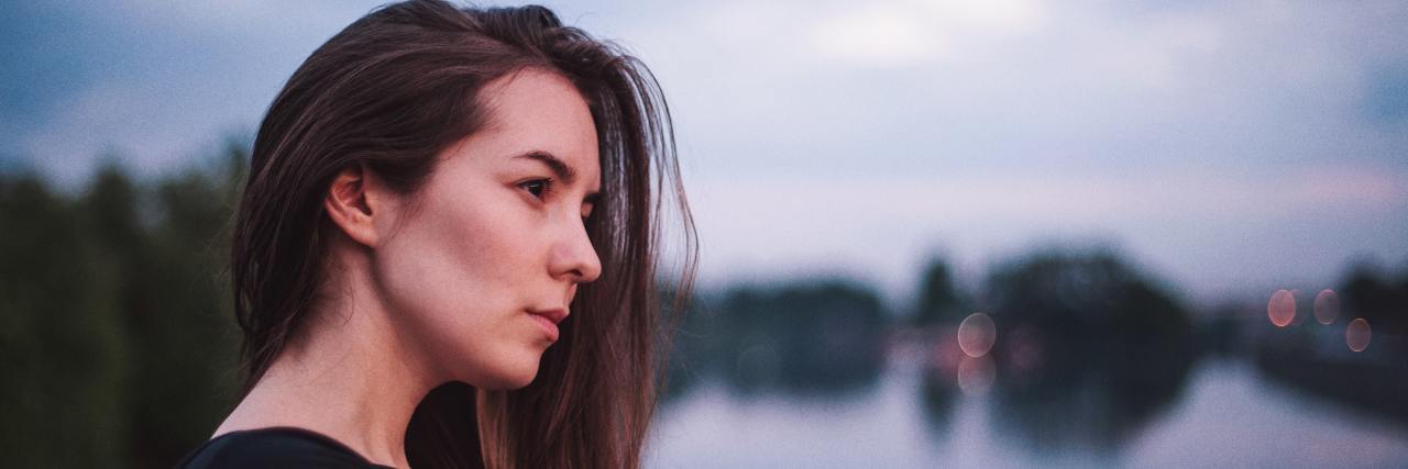 A woman with brown hair, thoughtfully looking out towards a body of water.