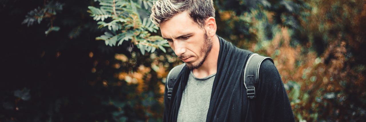 photo of man looking sad, down and away from camera, with blurred background of trees and leaves