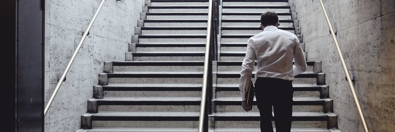 How Living With OCD Is Like a Full-Time Job back of a man in a white button down and black work pants walking up the stairs of a station to the street