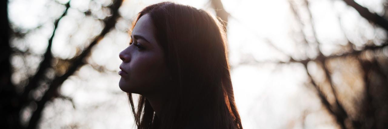 When Ignoring My Body Helps My Anxiety, but Hurts My Chronic Illness girl with straight brown hair in a forest looking to the side of the camera