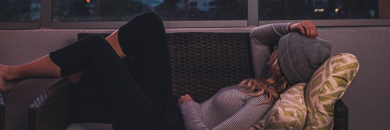 photo of woman lying on sofa on balcony at sunset with red sky in distance