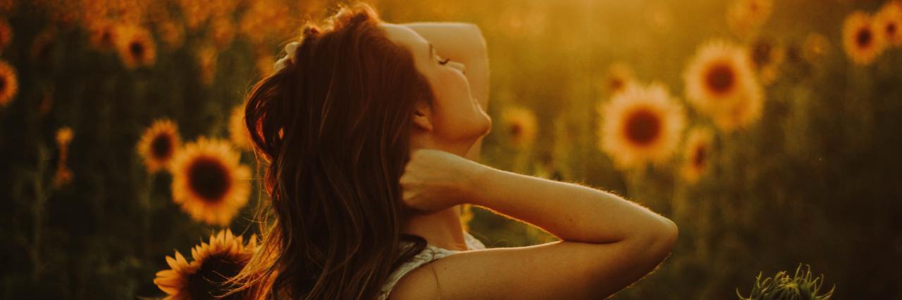 How I’ve Learned to Factor Chronic Illness Into My Future Woman standing in a sunflower garden at sunset.