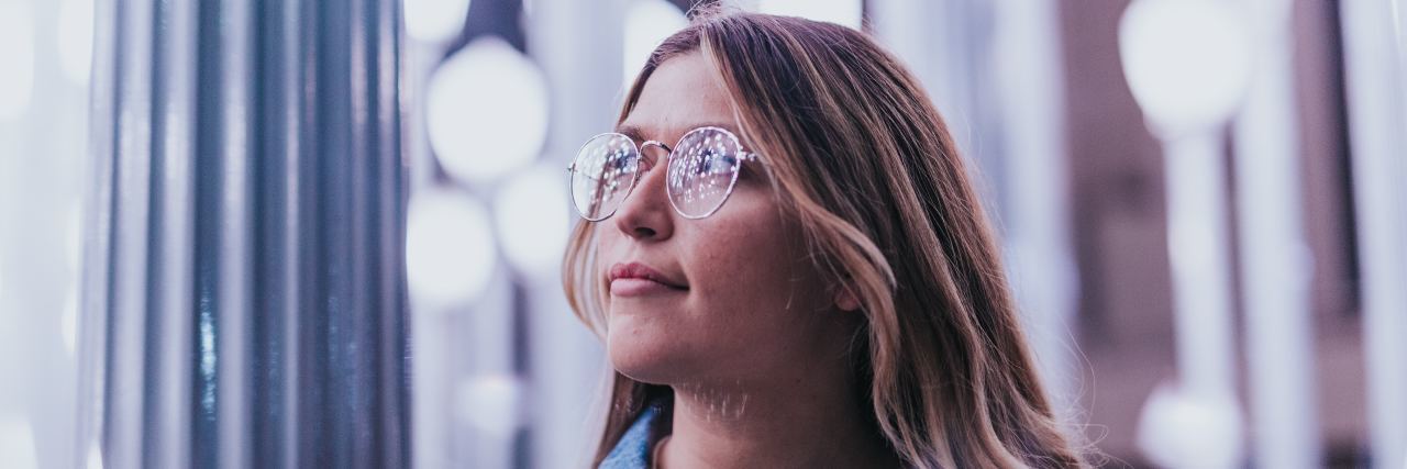 How I Find Meaning in Psychosis While Battling Different Realities young woman with blonde hair and glasses looking up with lights behind her