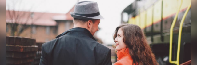 A man wearing a hat and a woman in a bright red/orange coat looking lovingly at each other
