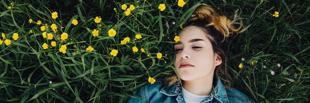 Woman laying in grass and flowers, wearing a jean jacket