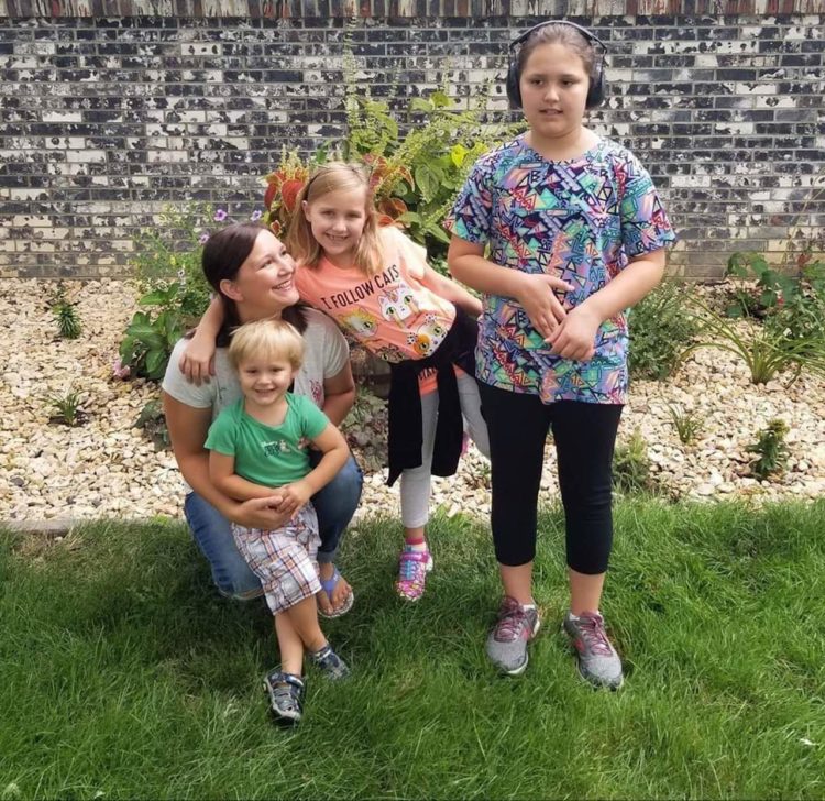 a mother posing for a picture on the grass with her three children.