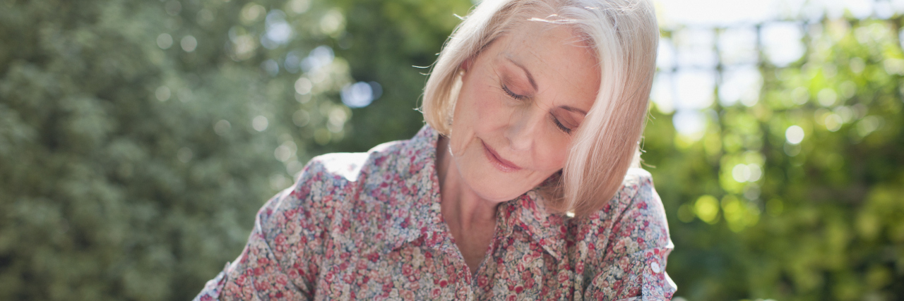 Why Saying 'I Live With Depression' Best Describes How I Relate to It older woman in flowered shirt sitting outside writing