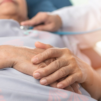 Hospitalized elderly patient, senior old aging woman laying on bed with cardiologist doctor or physician examining cardiological heart health, checking pulse in hospital clinic exam room