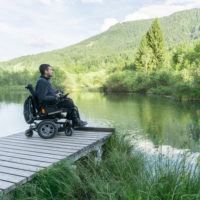 Man with Duchenne muscular dystrophy in power wheelchair on dock looking at lake.