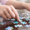 woman's hands putting pieces of a puzzle together on a table