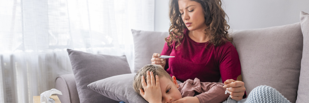 After COVID-19 Is Contained, We Should Still Prevent Spread of Illness A mom with her child on the couch. She's holding a thermometer after checking her child's temperature