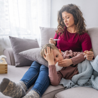 A mom with her child on the couch. She's holding a thermometer after checking her child's temperature