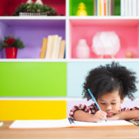 little girl in front of a colorful bookshelf writing on paper