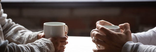 a close up of a woman and a man's hands each holding a coffee cup sitting at a table