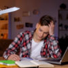 young man sitting at a desk doing homework, frustrated