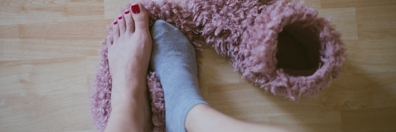 My Depression Is Thriving in COVID-19 Self-Isolation A woman in one sock putting on her slippers
