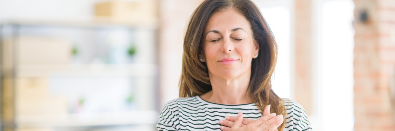 The Power of Feeling 'Seen' in the Midst of Mental Health Struggles woman in a striped shirt standing in a room with her eyes closed and hands over her heart