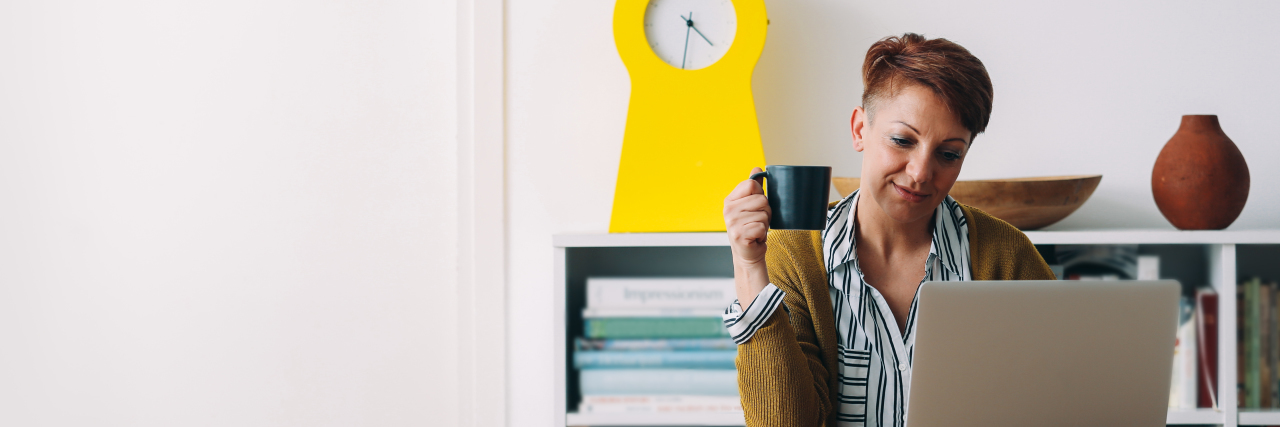 Talking About Suicide on Social Media Does Not Encourage It woman sitting at a desk on her laptop with a cup of coffee in her other hand