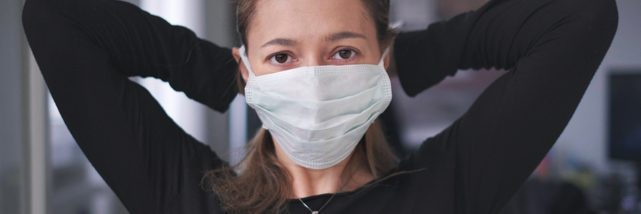 photo of woman attaching face mask to mouth while looking into camera with sad eyes