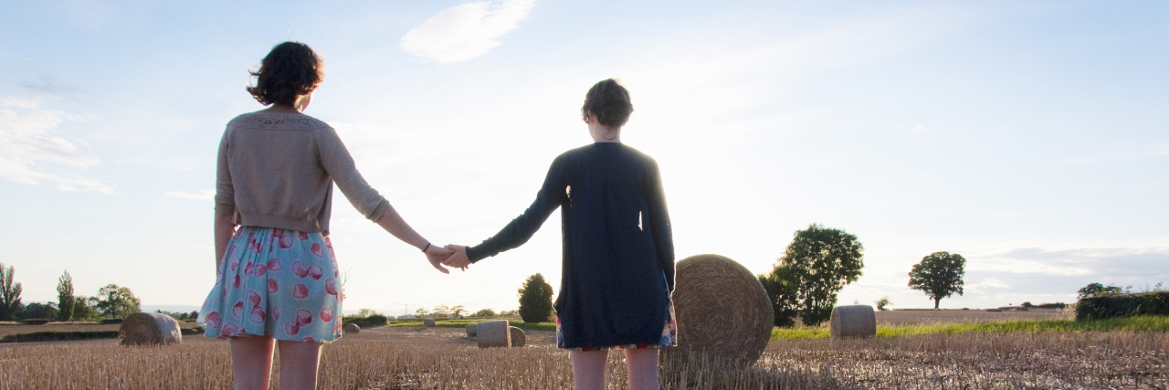 two girls holding hands outside in a hay field