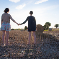 two girls holding hands outside in a hay field