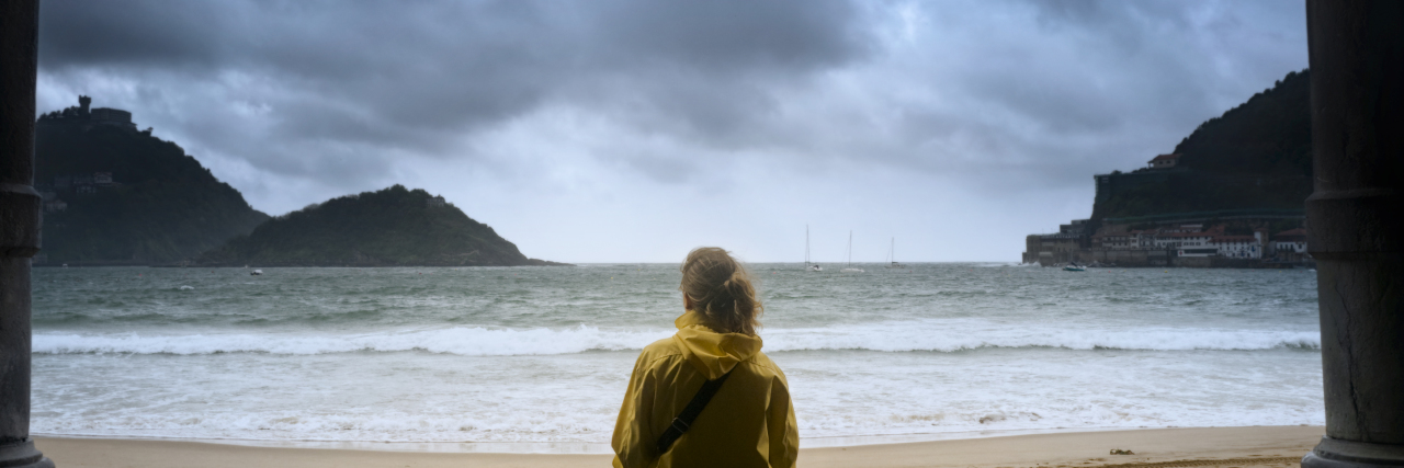 woman looking across ocean toward stormy horizon and mountains in distance