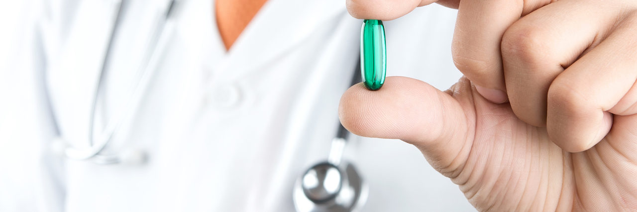 Close up of male doctor holding green pill