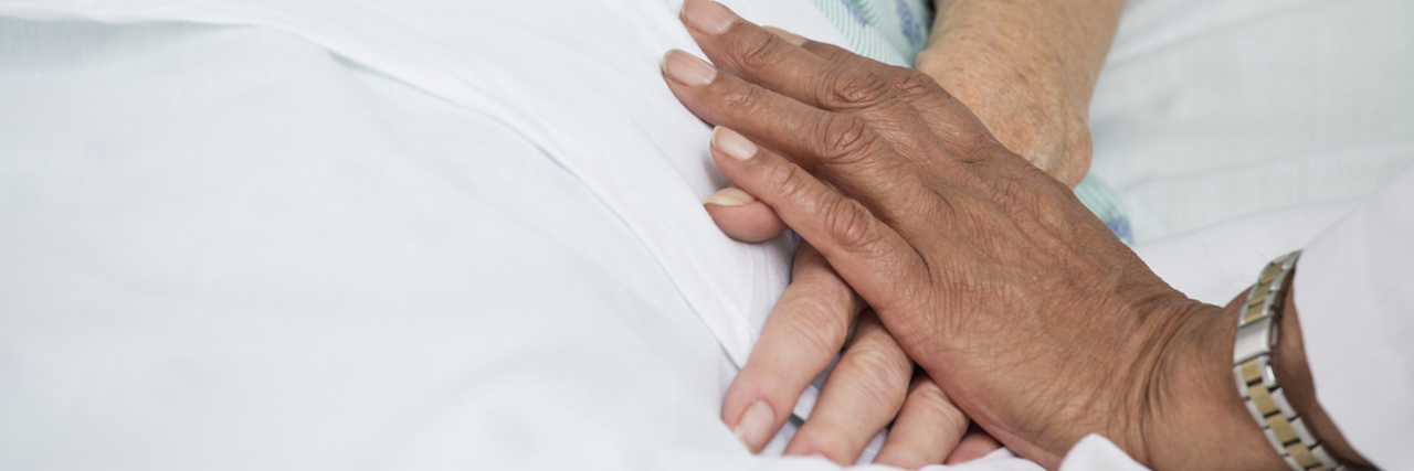 Resource Shortages May Cause Undue Suffering for Coronavirus Patients Doctor holding patient's hand in hospital.