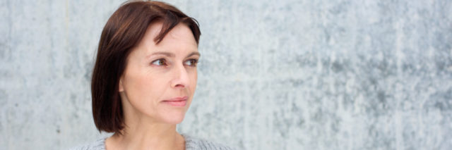 woman in a sweater standing against a gray wall looking away