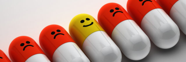 A row of pills with sad faces, with one with a smiley face in the middle