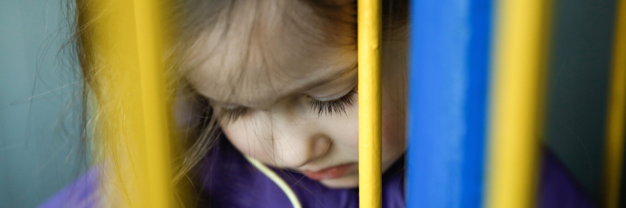 A young girl looking down behind a colorful fence