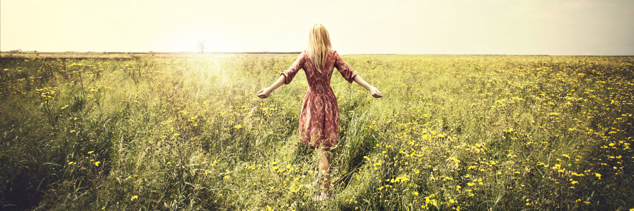 Woman walking towards sun in a field.