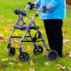 Woman using a rollator walker in grass with autumn leaves.