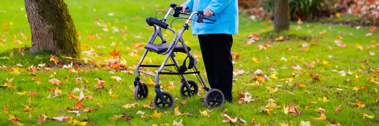 Woman using a rollator walker in grass with autumn leaves.