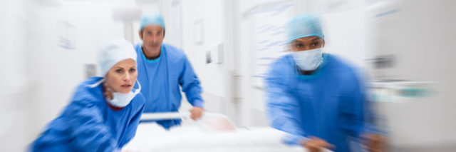Nurse and doctor in a hurry taking patient to operation theatre. Patient on hospital bed pushed from surgeon to emergency theatre. Team of doctors and surgeon rushing patient. (Nurse and doctor in a hurry taking patient to operation theatre. Patient o