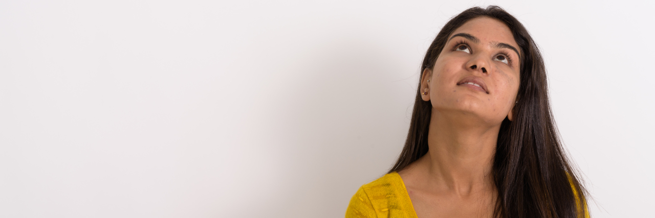 What It's Like to Have Anxiety in the Middle of the COVID-19 Pandemic woman in a yellow shirt with long, brown hair looking up