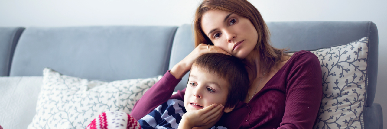 Mother holding son on the couch, looking worried.