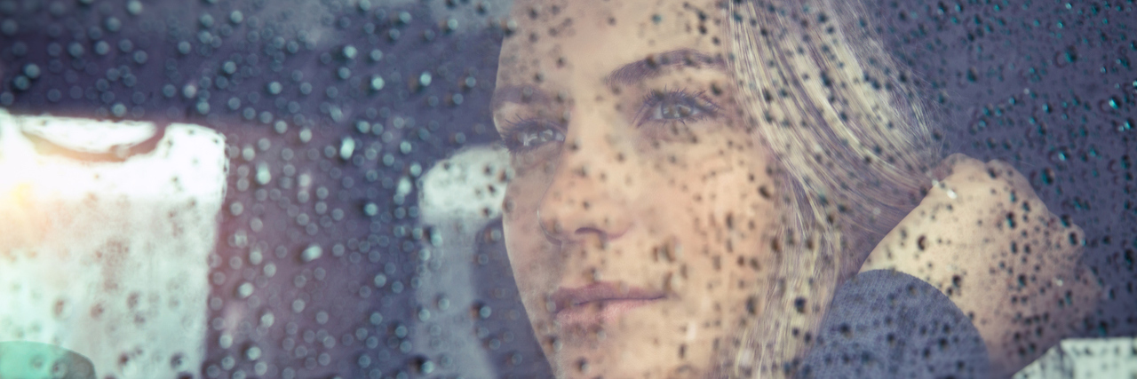 Woman sitting behind window with rain drops on it